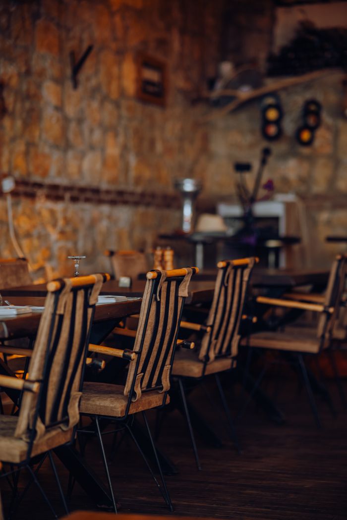portfolio-01 Rustic restaurant interior with empty wooden chairs set against a stone wall, creating a cozy dining atmosphere.